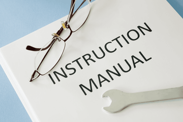 Book titled 'INSTRUCTION MANUAL' with glasses and a wrench on a light blue background