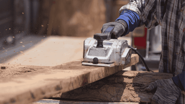 Person using a power planer on a wooden surface with a blurred background